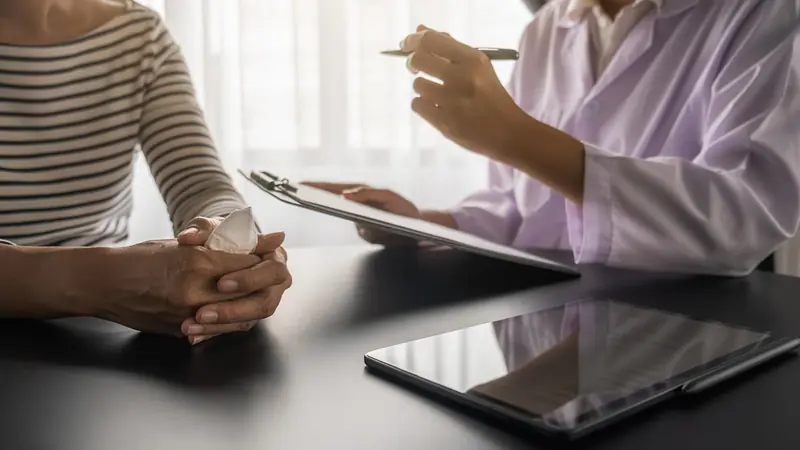 A care consultant taking notes on a clipboard while listening to a family member across a table.