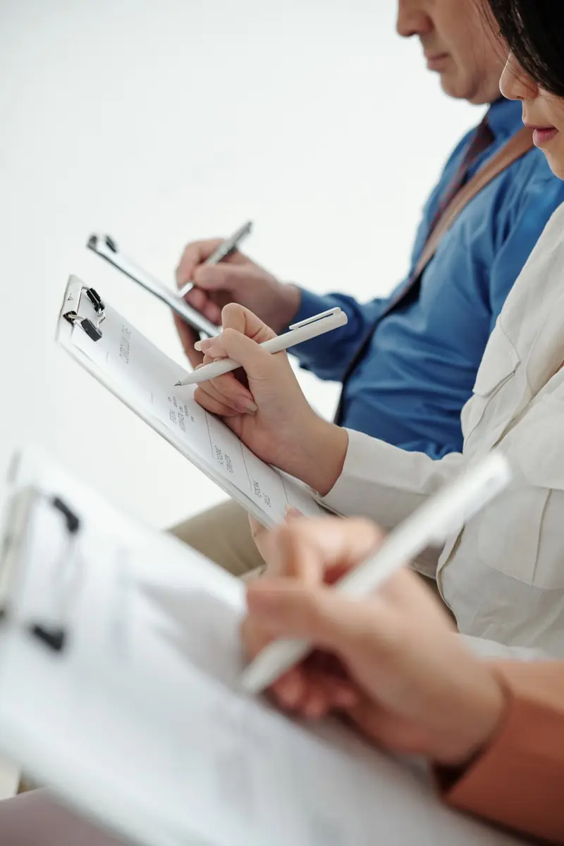 Two people filling in assessment forms on clipboards during a care evaluation.